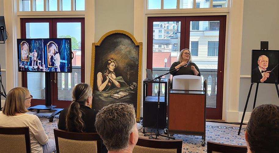 A woman presents a talk at a Luminaries event featuring several artistic representations of opera.