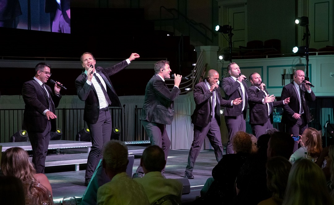 Wearing dark suits, the nine members of Straight No Chaser dance and sing on the Palladium stage.