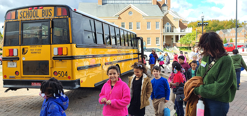Students and teachers exit a school bus and line up to enter the Palladium.