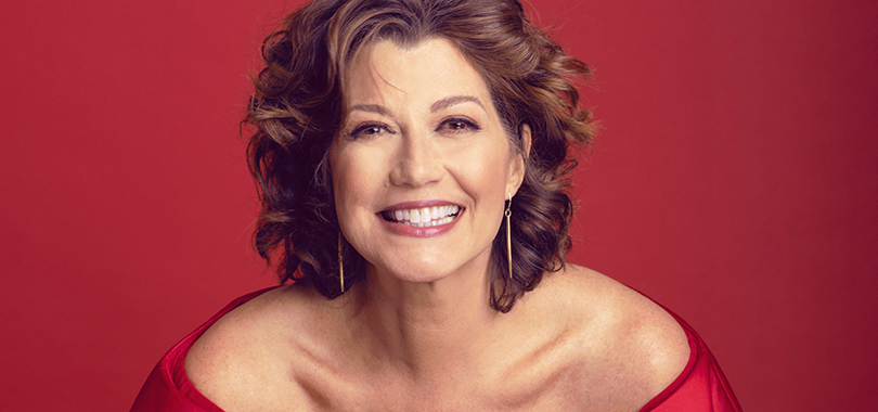 Amy Grant grinning in a red top against a bright red background.