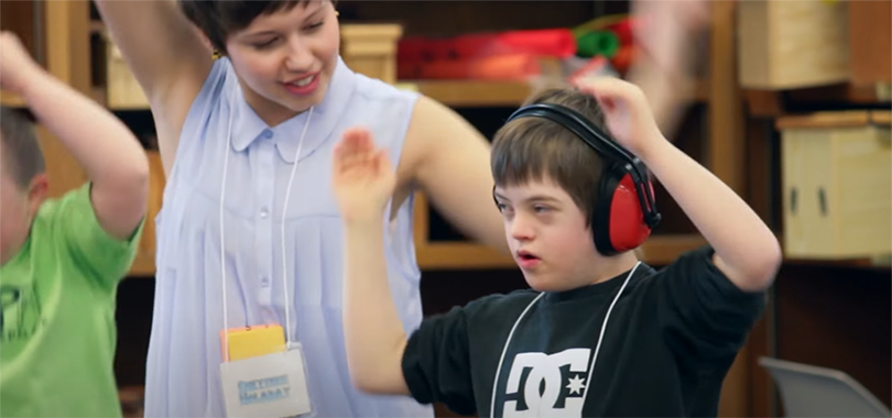 A female college student practices a dance with a disabled boy