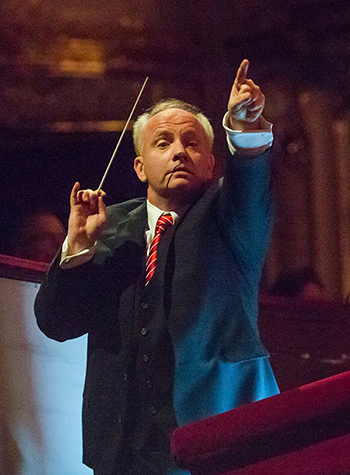 Conductor Theodore Kuchar, a white-haired man wearing a dark suit, gestures with his baton.