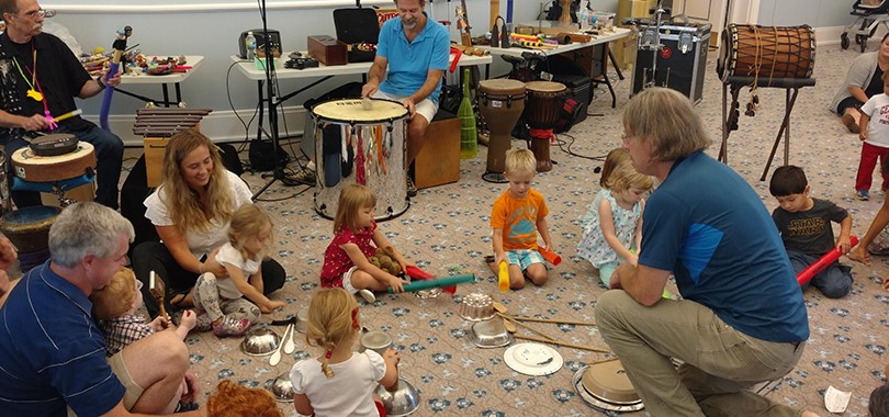 Children and their parents gather around the floor to play with various percussion instruments, including bowls and spoons.
