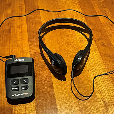 A black handheld device is connected to a set of headphones on a wooden counter.