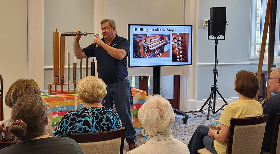 A man demonstrates the functions of a pipe organ stop with a screen behind him reading "Pulling out all the stops".