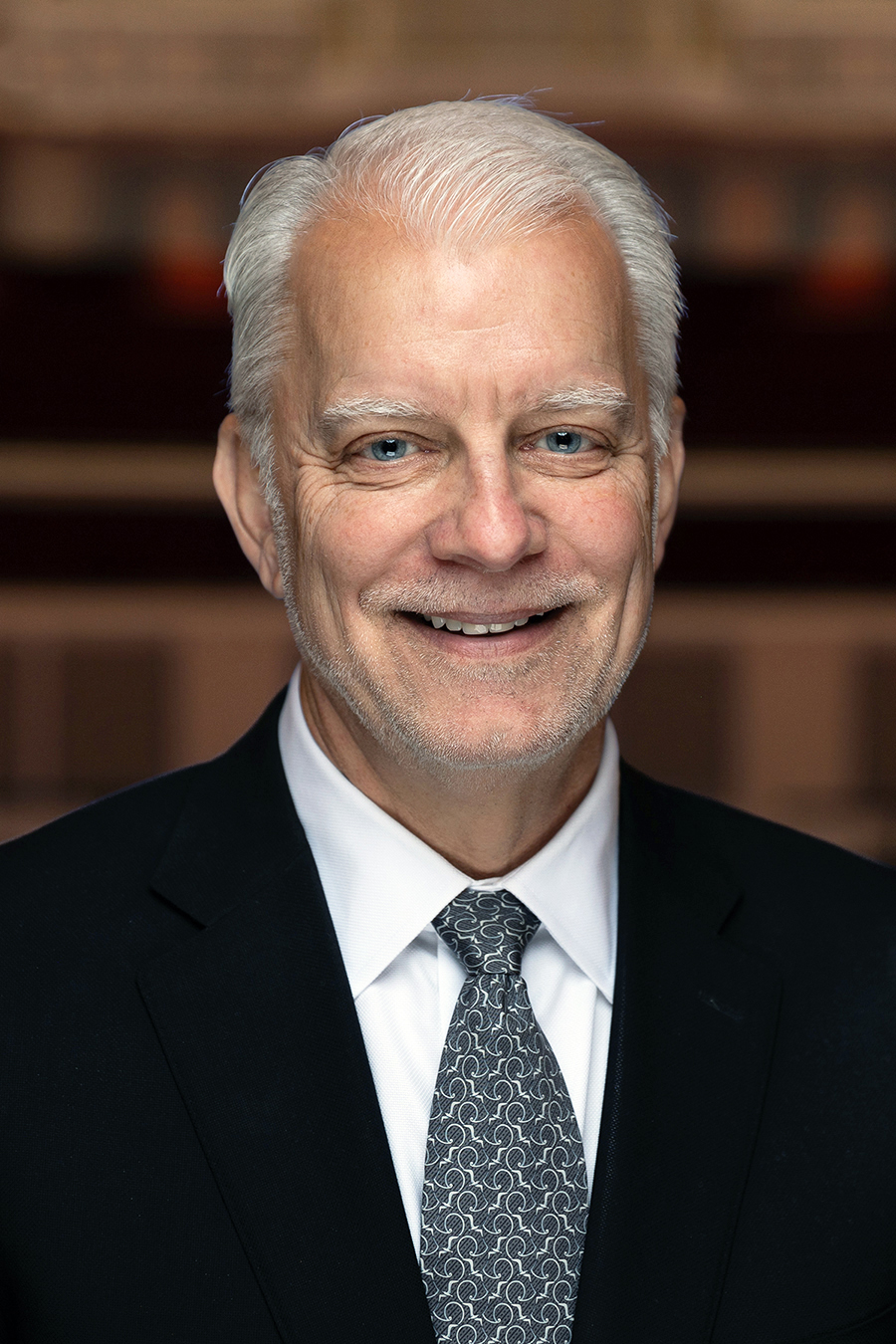 A white-haired man in a dark suit smiles for a photo