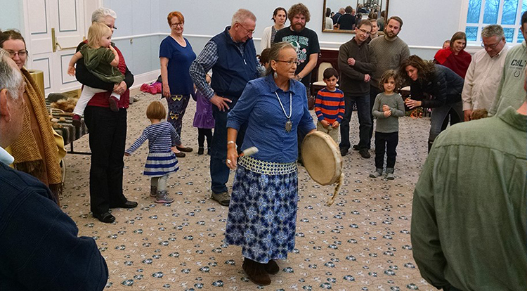 Native American storyteller Teresa Webb plays a drum amid a circle of people.