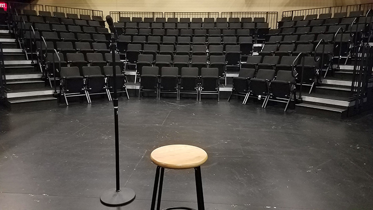A microphone stand and a stool sit in an empty theater.