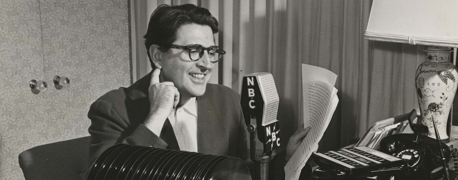 A man reads a script into an old-fashioned NBC radio microphone.