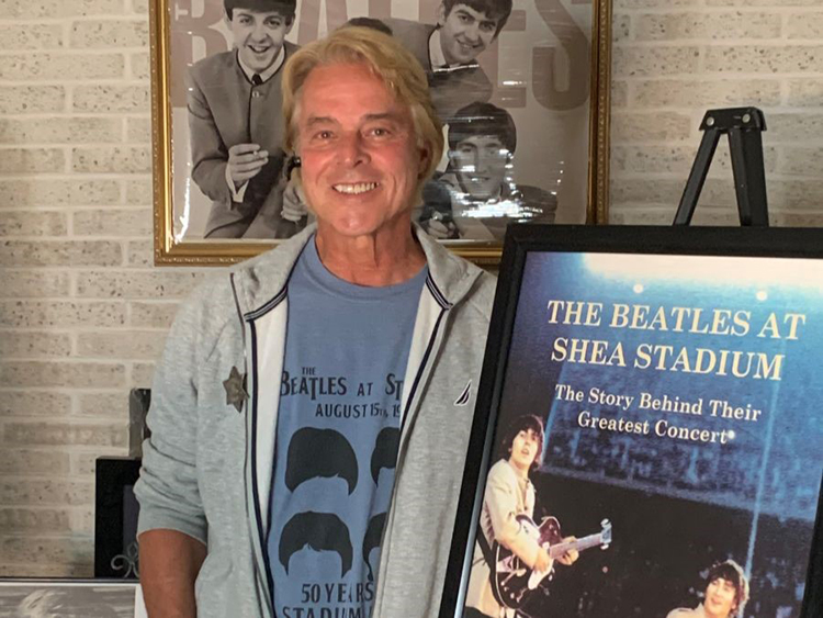 Author Dave Schwensen stands near a poster of the Beatles.