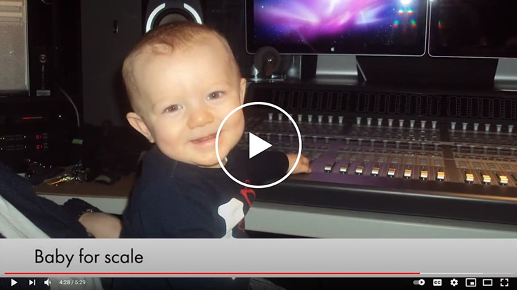A smiling baby sits at an audio mixing board