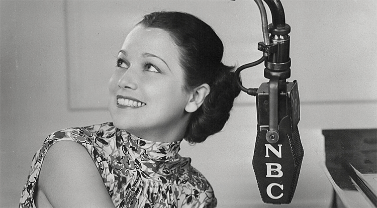 A smiling woman sits at an NBC radio microphone.