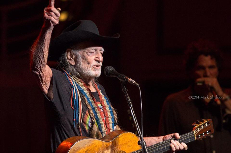 Country star Willie Nelson plays an acoustic guitar on stage.