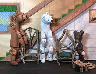 Three wooden marionettes – a brown bear, a polar bear and a mouse – stand on a lodge-like set.