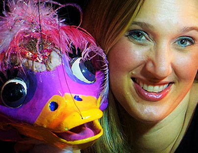 Closeup of a smiling woman holding a purple duck marionette.