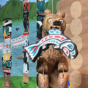 A wooden bear puppet catches a wooden fish amid colorfully painted totem poles