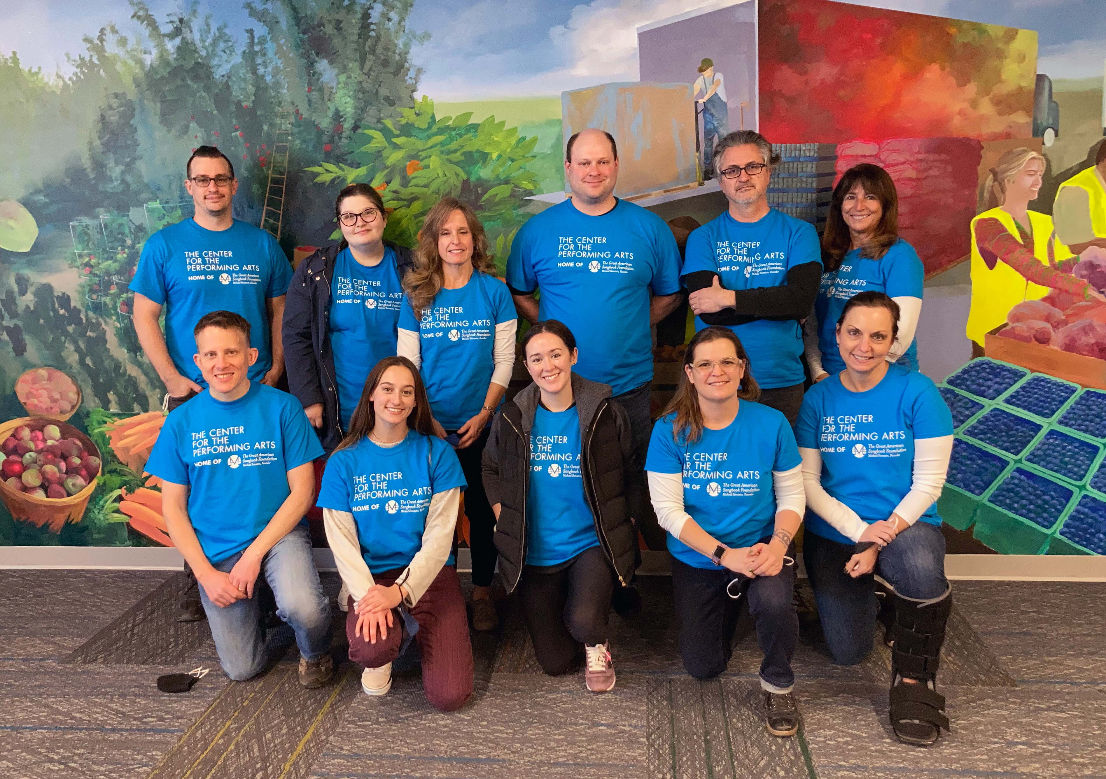 Eleven people in blue T-shirts pose against a painted mural.