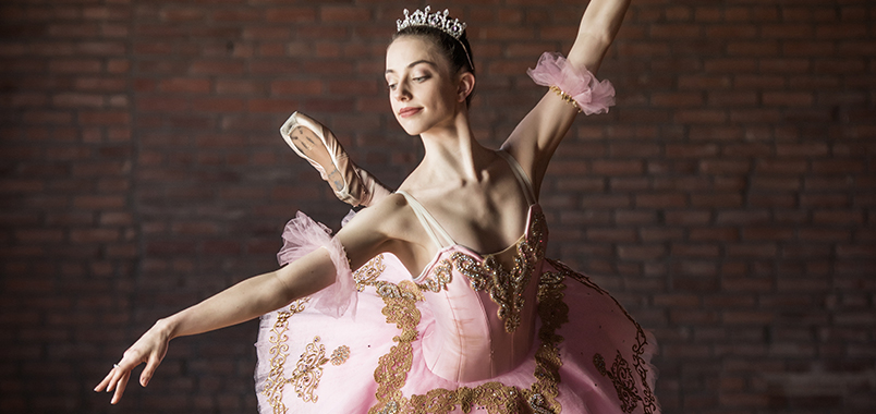A ballerina poses in arabesque wearing an intricately embroidered dress and a jeweled tiara.