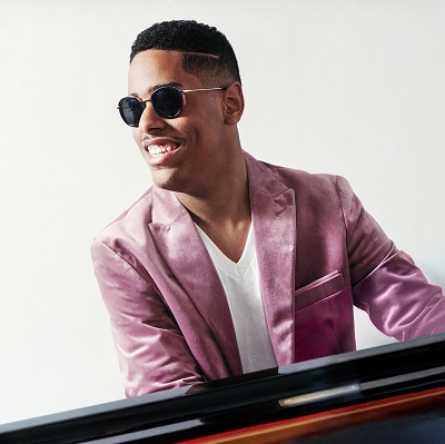 A man in sunglasses and a sportcoat plays a piano.