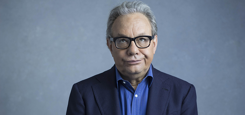 Lewis Black, a white man in his 70s, rolls his eyes and smirks in a portrait pose.