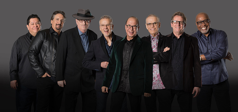 Tower of Power Tower of Power, a diverse group of eight men, pose in a line against a gray background.