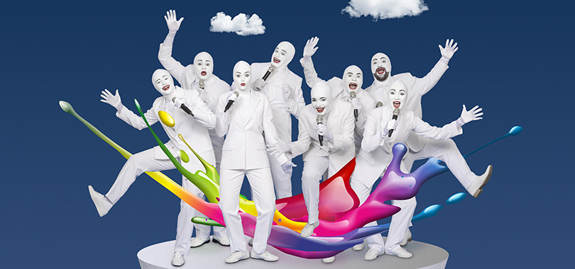 Eight people dressed all in white, with white face paint and bright red lipstick, sing into microphones and pose with their arms or legs stuck out. A rainbow-colored splash effect is at their feet.