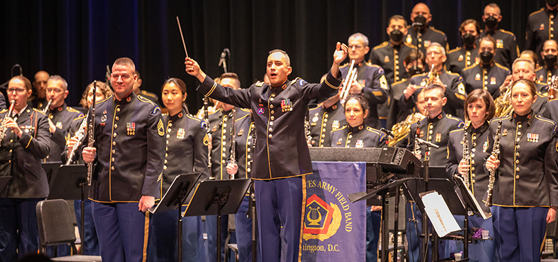 The members of the U.S. Army Field Band perform in uniform. The conductor faces out towards the audience.