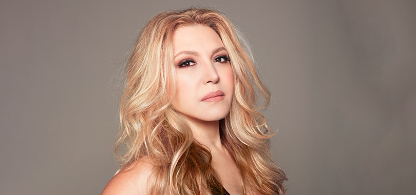 Eliane Elias, a Brazilian woman in her 60s, has long wavy blond hair and poses against a smoky gray background.