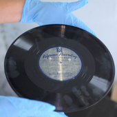 An antique record held by a person wearing blue gloves