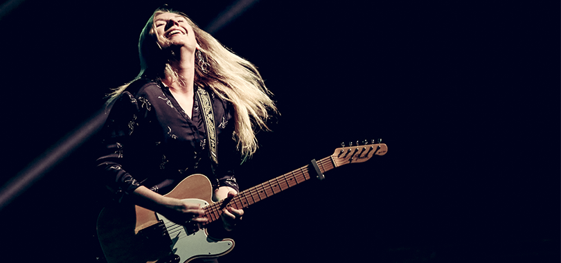 Joanne Shaw Taylor plays electric guitar lit by a spotlight.
