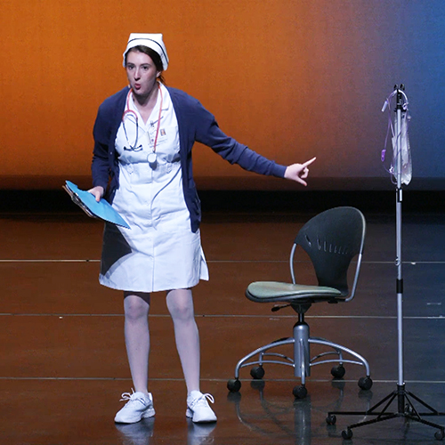 An actress dressed as a nurse gestures on stage.