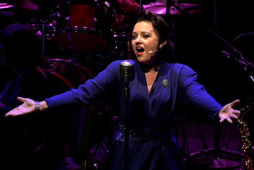 A woman in a blue dress sings onstage.