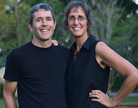 A woman and a man dressed in black pose smiling together outdoors.