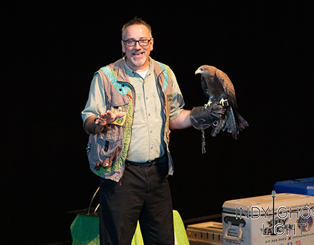 A man dressed in a safari outfit demonstrates a hawk perching on his gloved hand.