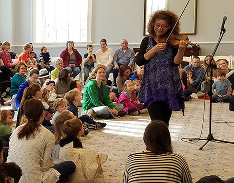 Cathy Morris plays electric violin in front of a room filled with kids and parents.