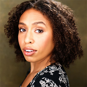 A black woman in a floral dress looks over her should at the camera.