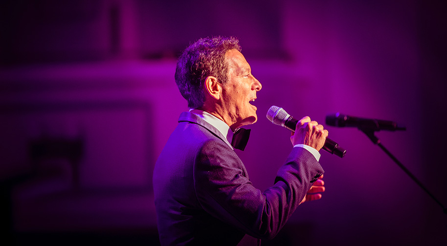Michael Feinstein singing wearing a navy and black tuxedo.