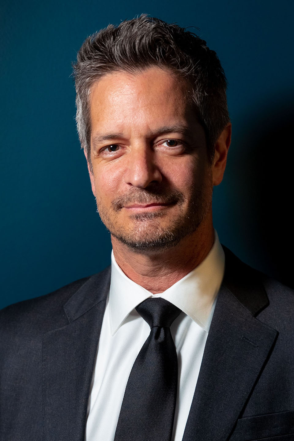 A man wearing a dark suit and tie smiles forthe camera