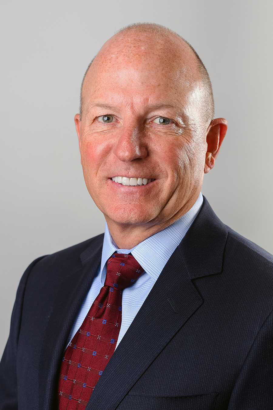 A man in a dark suit and red tie smiles for a photo.