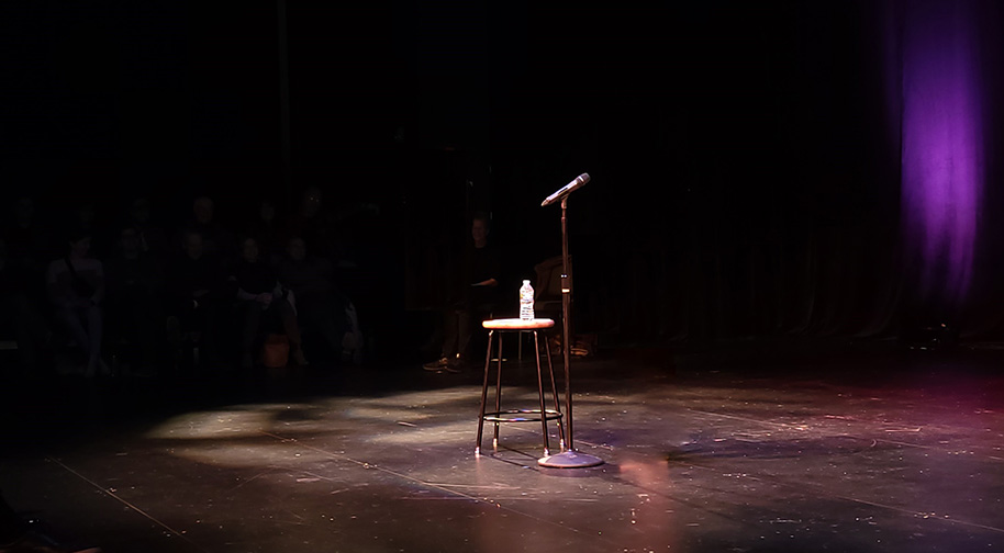 A microphone stand next to a stool with a bottle of water on an empty Studio Theater stage.