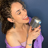 A woman in a purple dress closes her eyes and sings into a microphone.
