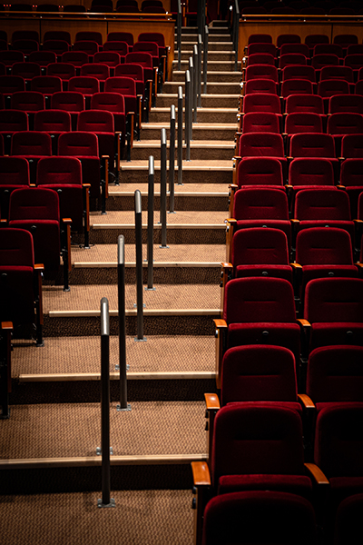 New steel handrails line the aisle of a stadium-style theater with red seats.