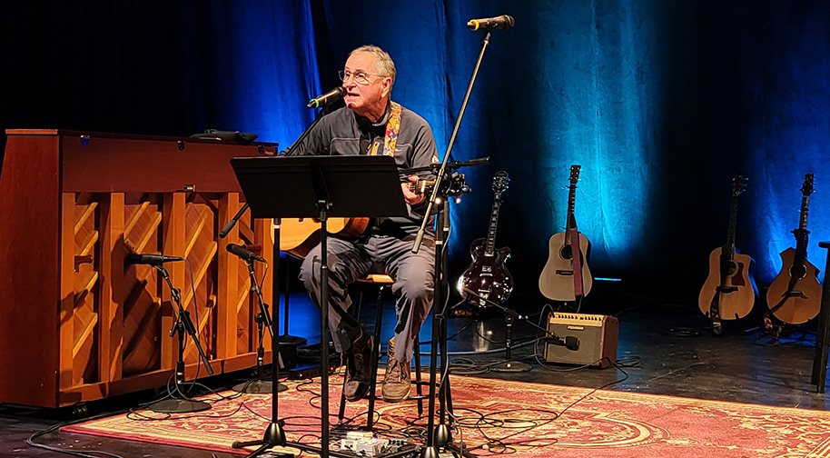 Songwriting 2025 914X504 2 A man sits and plays guitar at the Songwriters in the Round performance.