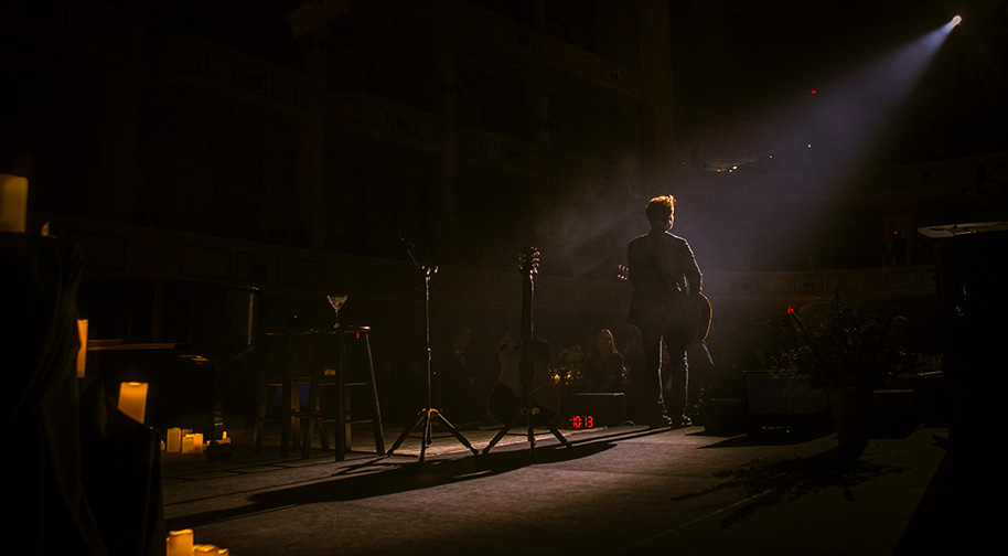 Richard Marx performs under a single blue spotlight surrounded by lit candles.