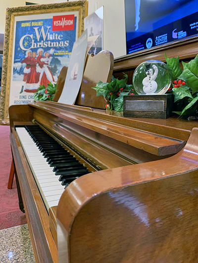 An upright piano is decorated with a holiday movie poster and Christmas knickknacks.